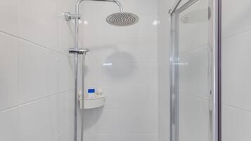 A modern shower enclosure with a handheld showerhead, a glass door, and a small shelf with toiletries.