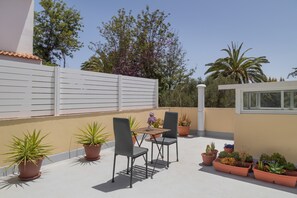 Une terrasse sur le toit, avec une table et deux chaises, entourée de plantes en pot.