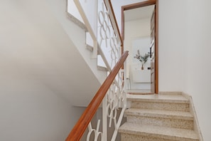 Una escalera con barandilla de madera y un pasamanos decorativo blanco, que conduce a una habitación con pared blanca y una planta en maceta.