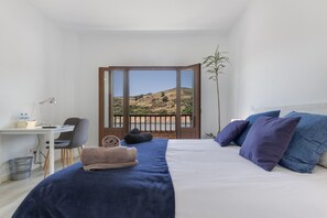 Une chambre à coucher comprenant un lit, un bureau, une chaise, une plante et une vue sur un paysage, visible à travers une porte.
