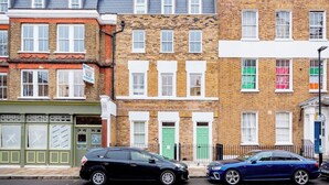 A row of terraced houses with distinct front doors and windows, parked cars, and a clear sky. - Angel Brand New Penthouse (Greater London)