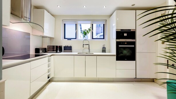 A modern kitchen with white cabinetry, a built-in oven, a microwave, and a sink. - The Liverpool Trendy House (Greater London)