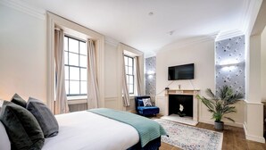 A bedroom with a large bed, a blue armchair, a fireplace, and a TV mounted on the wall. - The Liverpool Trendy House (Greater London)