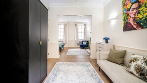 A hallway with a dark wardrobe, a light-colored sofa with decorative pillows, and a colorful painting on the wall. - The Liverpool Trendy House (Greater London)