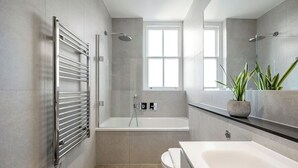 A modern bathroom with a glass-enclosed shower, a large mirror, and a potted plant.