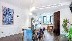 A modern kitchen with white cabinets, a glass island, and a dining area with a glass table and blue chairs. - Deluxe and Peace in Primrose Hill (Greater London)