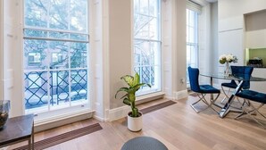 A modern room with large windows, a dining area with blue chairs, and a potted plant.