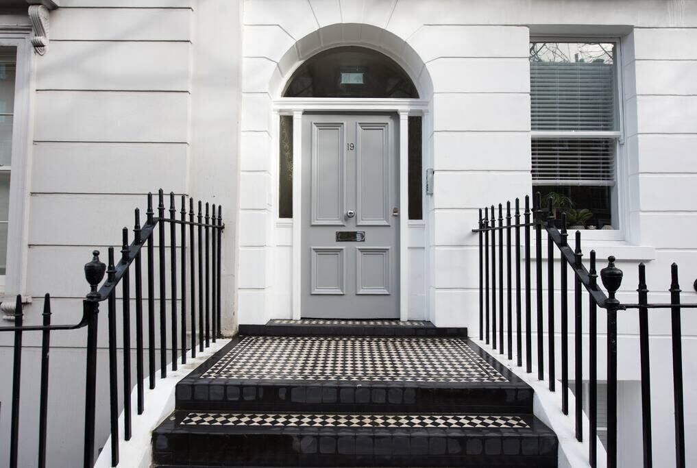A white building with a grey door, black iron railings, and a tiled entrance.