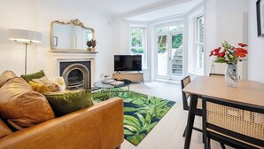 A modern living room with a fireplace, a television, and a dining area with a table and chairs. - Bloomsbury Gardened 2 bedFlat (Greater London)