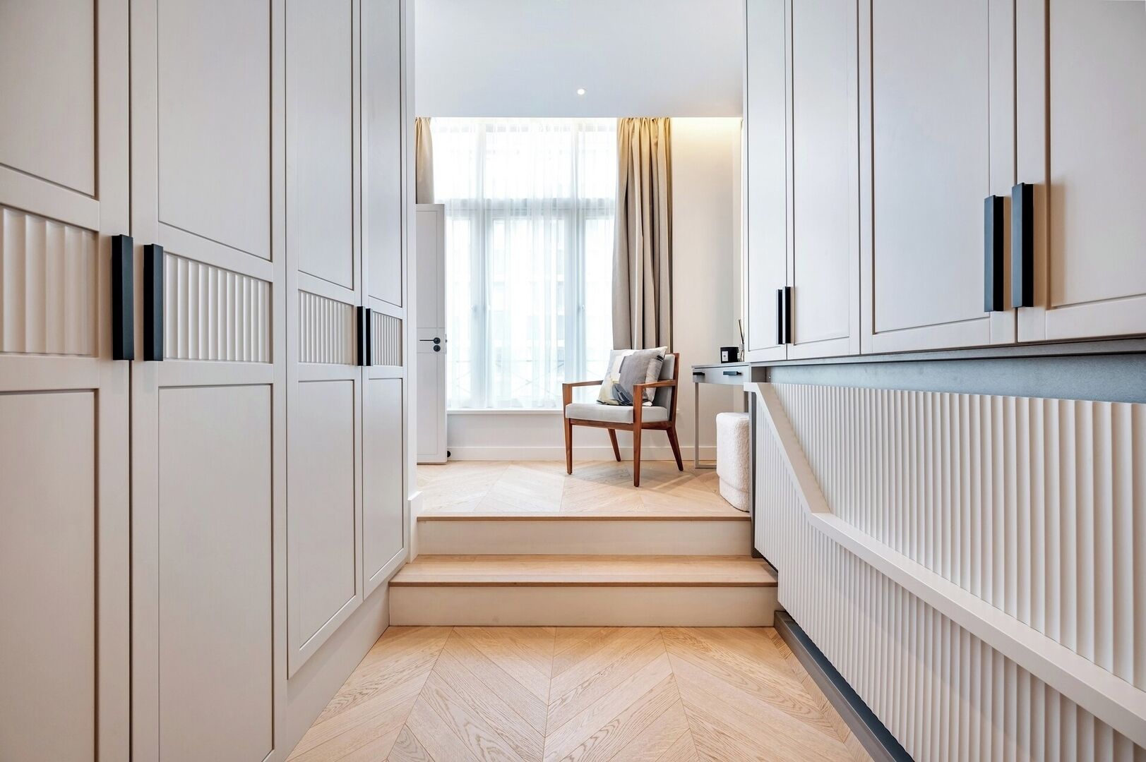 A modern interior with a staircase leading to a seating area, featuring a chair and a table.