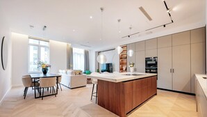 A modern kitchen with a central island, wooden cabinets, and a dining area with a table and chairs. - West end Deluxe flat N.2 (Greater London)