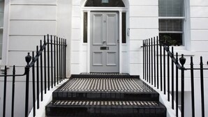 A white building with a grey door, black iron railings, and a tiled entrance.
