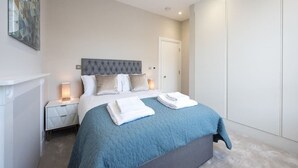 A bedroom with a large bed, a nightstand, a wardrobe, and a painting on the wall.