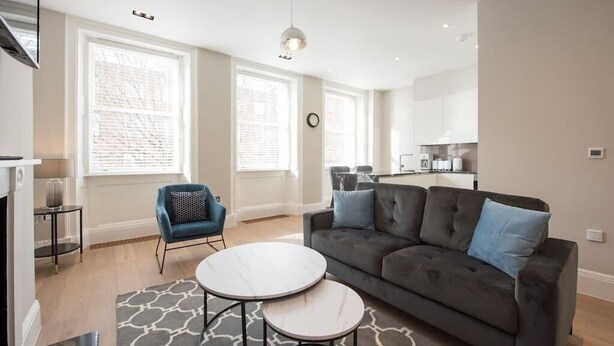 A modern living room with a grey sofa, two round tables, and a blue armchair.