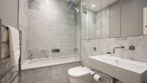 A modern bathroom with a glass-enclosed shower, a white bathtub, a toilet, and a sink with a small plant on the counter.