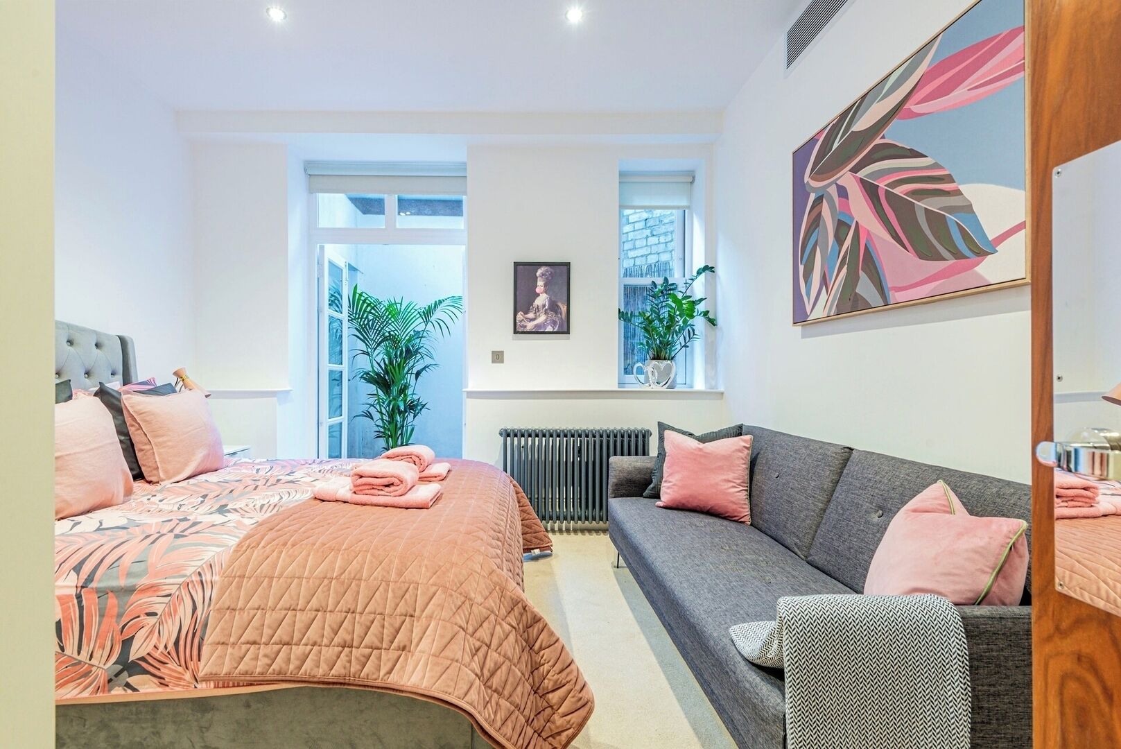 Une chambre moderne avec un lit, un canapé et un radiateur. On y trouve également des plantes et un tableau accroché au mur.