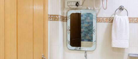 Un baño con puerta de madera, un lavamanos blanco, un espejo, un perchero para toallas y un calentador de agua.