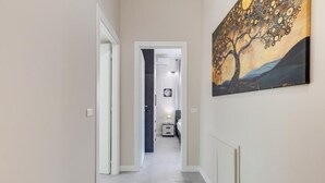 Ein Flur mit einem Gemälde an der Wand, einem Bett in der Ferne und einer Tür zu einem anderen Zimmer.