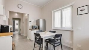 Eine moderne Küche mit weißen Schränken, einem Esstisch mit Stühlen und einem Fenster, das für natürliches Licht sorgt.