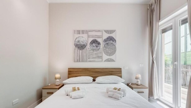 Ein Hotelzimmer mit einem großen Bett, zwei Nachttischen mit Lampen, einem Wandbild und einem Fenster mit Vorhängen.