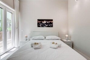 A hotel room with a bed, two bedside tables with lamps, a painting on the wall, and a view through the window. - Eco Domus Moon (Roma)