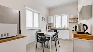 Une cuisine compacte avec un coin repas, des meubles blancs et une machine à café.