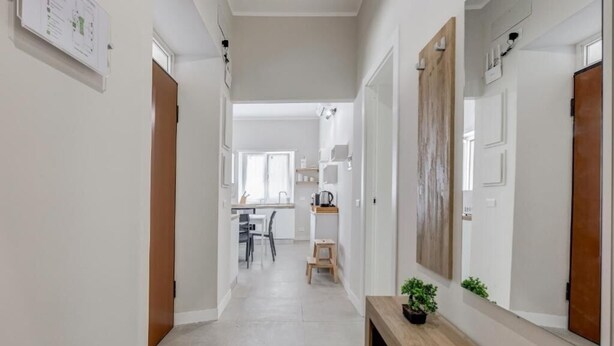 Un couloir avec un banc en bois, une petite table sur laquelle est posée une plante, et une porte sur la droite.