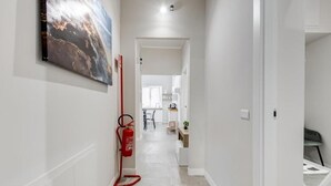 Un couloir avec un extincteur, un tableau et une vue sur un coin cuisine.