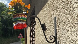 Eine Wandblumenampel mit gehäkelten Blumen, eine Metallhandläufe und ein Fußgängerübergang-Schild.