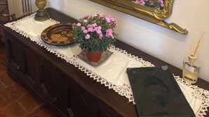 Ein Zimmer mit einem großen, verzierten Spiegel, einem Holzschrank, einer weißen Tischdecke aus Spitze und einem Blumentopf mit rosa Blüten.
