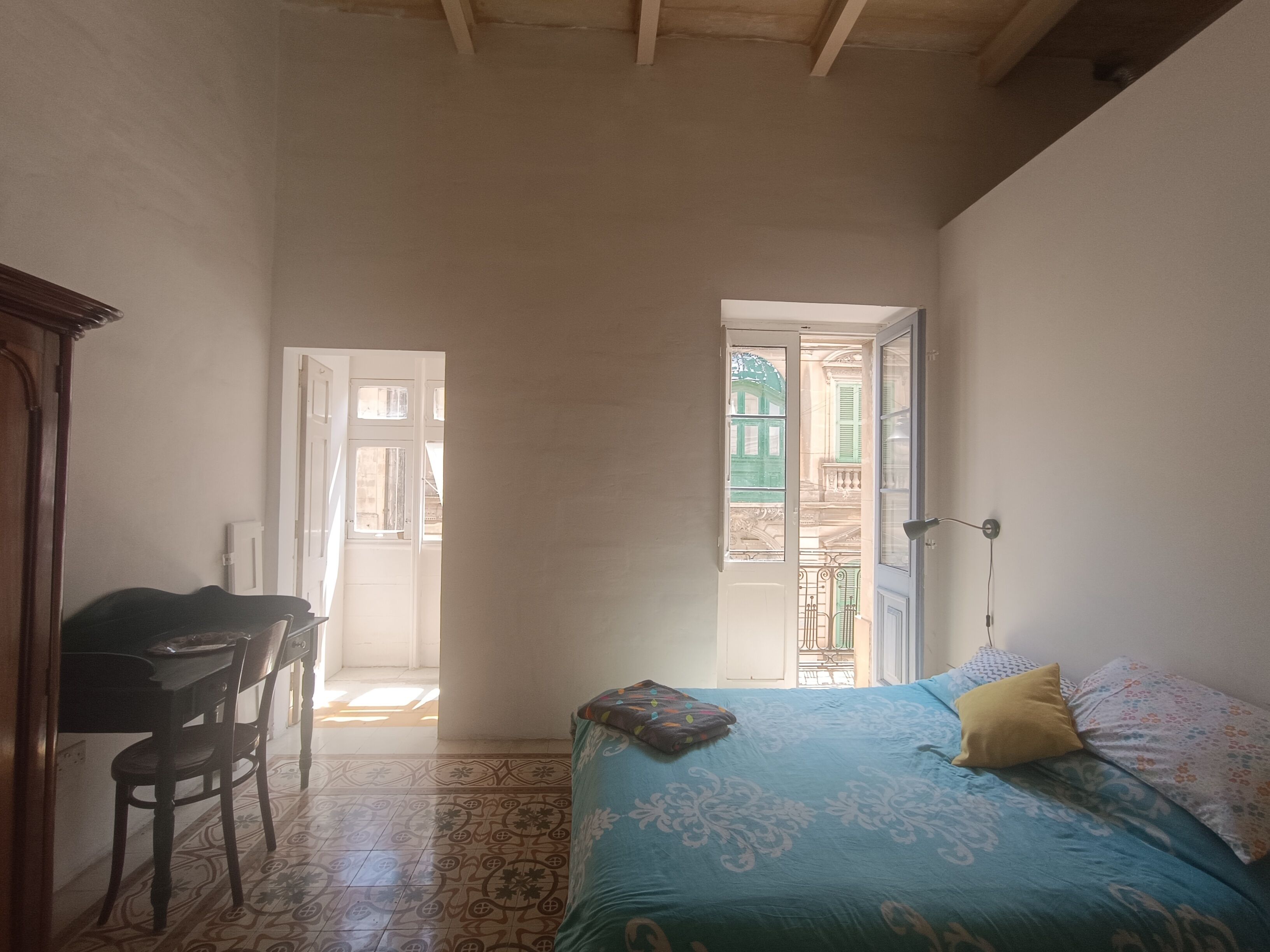 Une chambre à coucher avec un lit, une chaise et un bureau. Deux portes donnent sur l’extérieur.