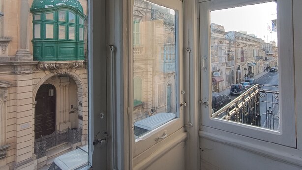 A corner of a room with a view of a street and buildings. - Charming Maltese townhouse (Il-Mosta)