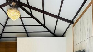 A room with a high ceiling, a bed, a TV mounted on the wall, and two chairs. - SRK Farm and Resort (Anjar)
