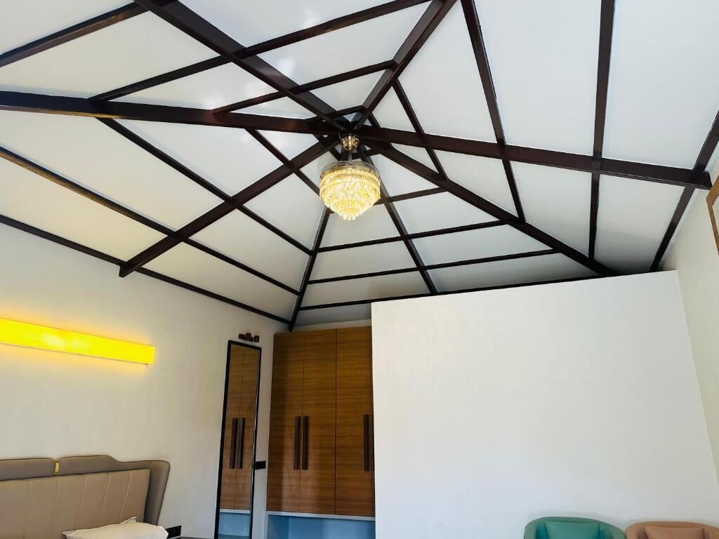Quarto com design geométrico no teto, um candelabro, uma cama, um guarda-roupa e uma luminária na parede.