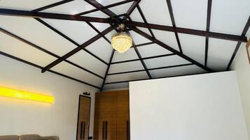 Quarto com design geométrico no teto, um candelabro, uma cama, um guarda-roupa e uma luminária na parede.