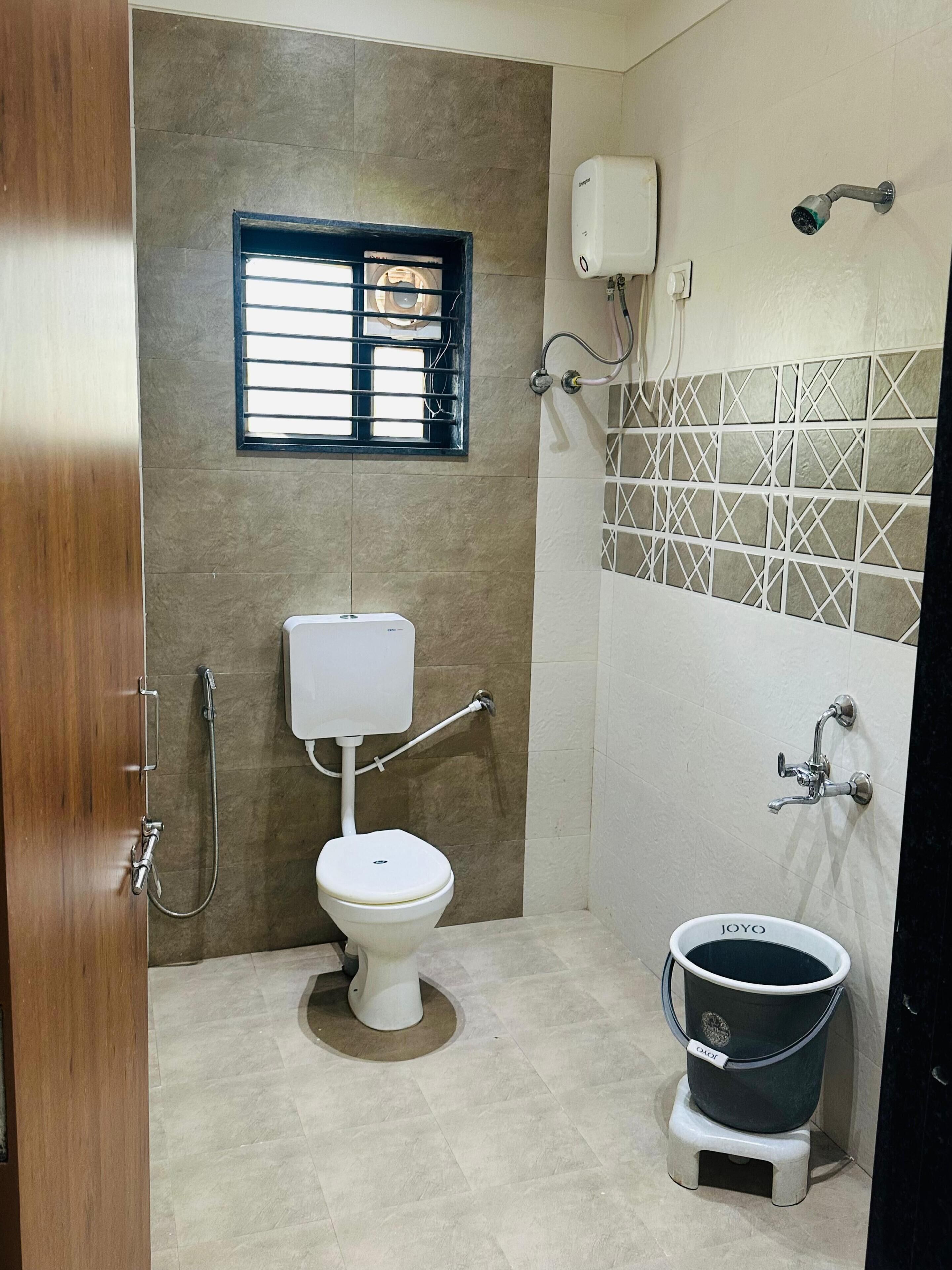 A bathroom with a toilet, a shower, a hand dryer, and a bucket.