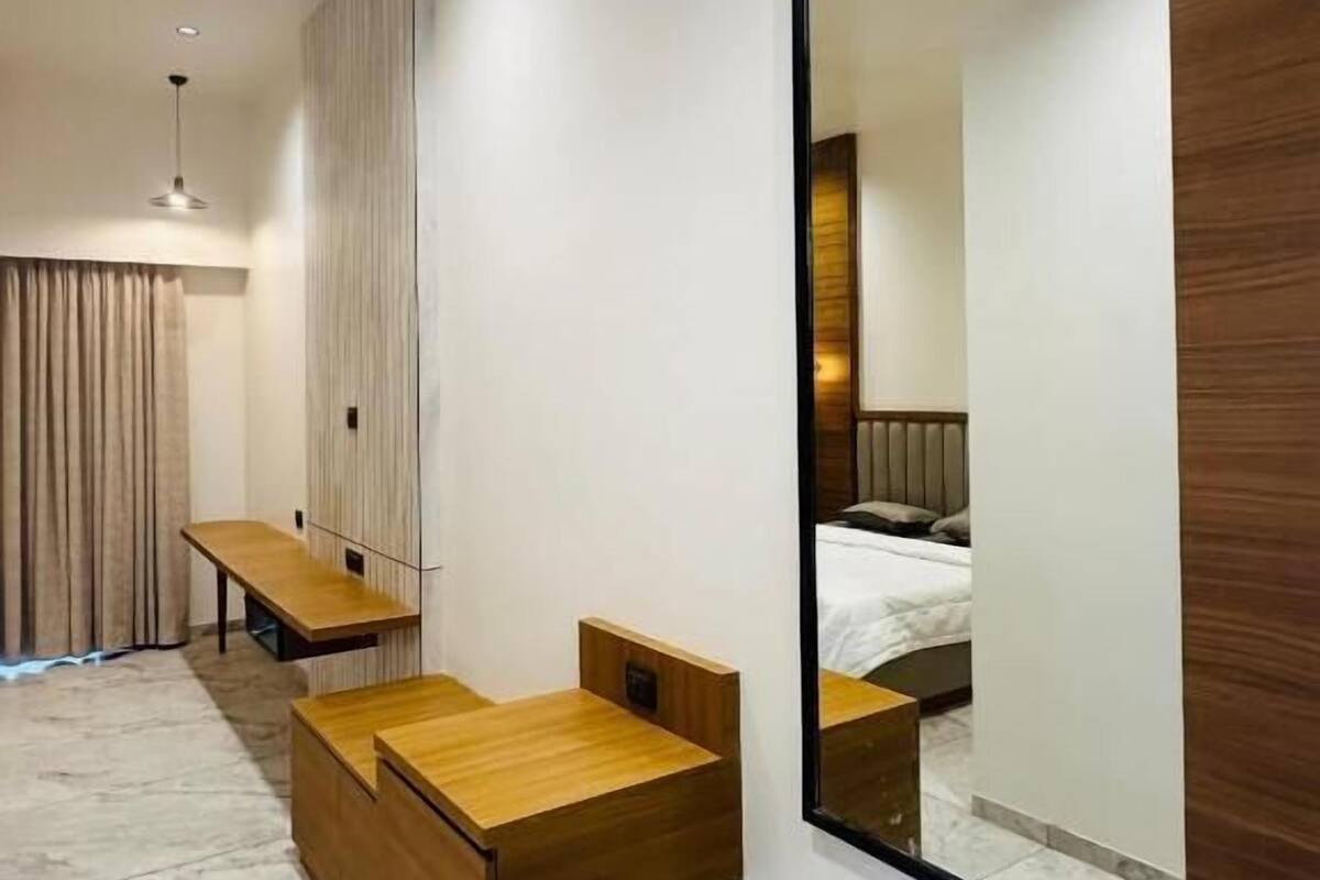 A modern hotel room with a large mirror, wooden furniture, a bench, and a bed.