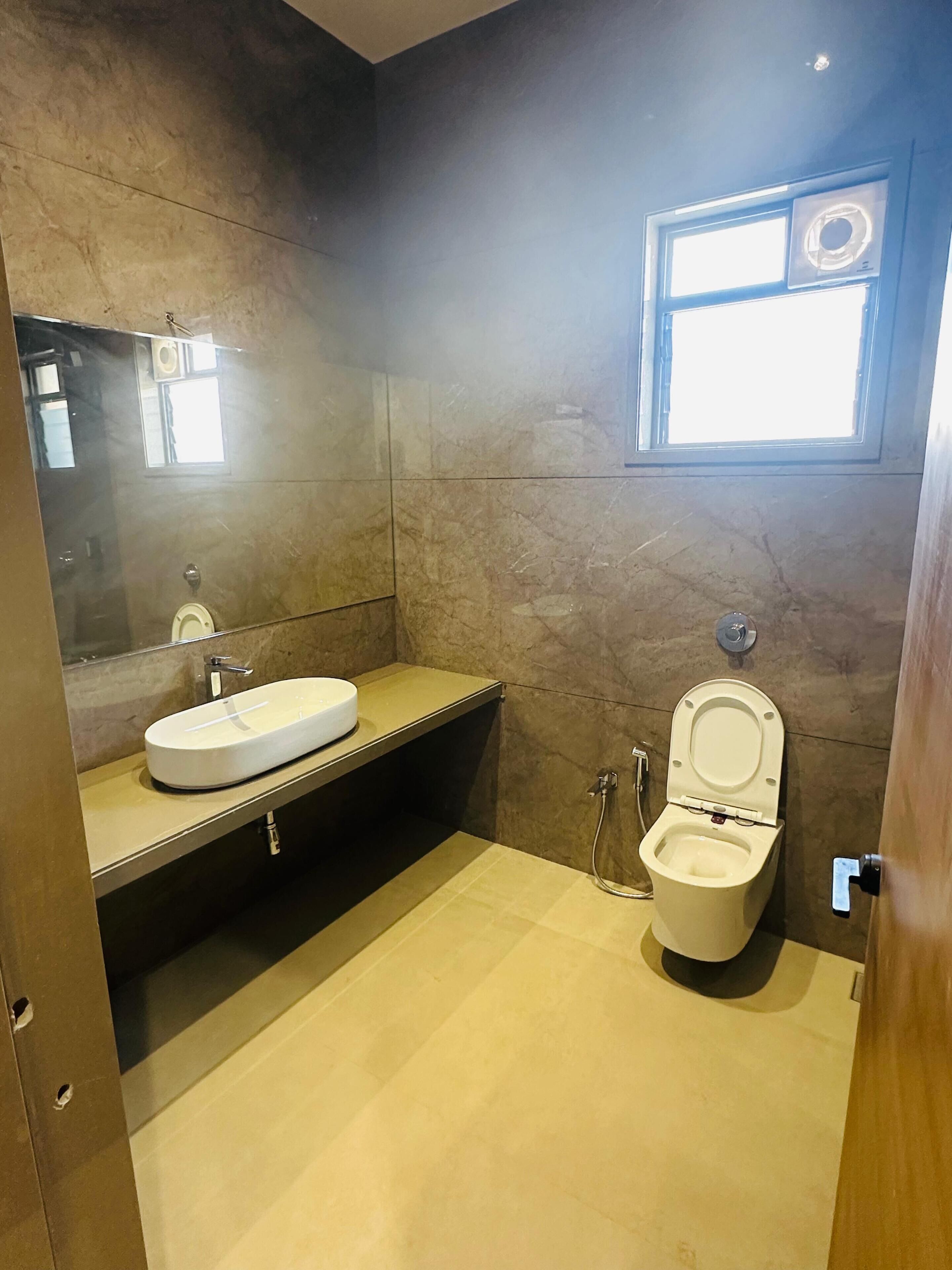 Un bagno con un lavandino bianco, un water, uno specchio e una finestra.