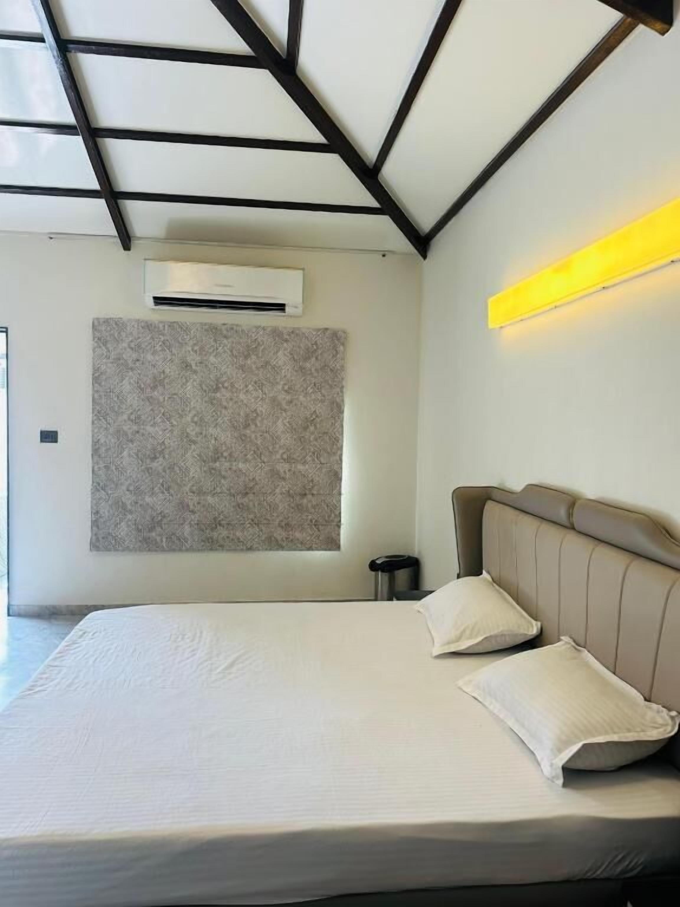 A bedroom with a bed, headboard, bedside table, and a wall-mounted air conditioner.