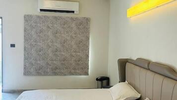 A bedroom with a bed, headboard, bedside table, and a wall-mounted air conditioner.
