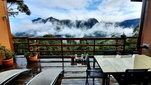 Een terras met uitzicht op bergen en wolken, met houten meubilair en planten in potten.