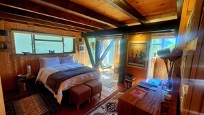 Ein gemütliches Blockhauszimmer mit einem großen Bett, einem kleinen Schreibtisch und einem Fenster mit Blick auf Grünflächen.