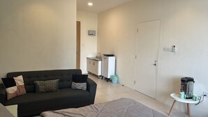 Een moderne woonkamer met een donkere bank, een bed, een klein keukentje en een deur.
