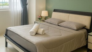 Een hotelkamer met een bed, een nachtkastje met een lamp, een schilderij aan de muur en een raam met gordijnen.