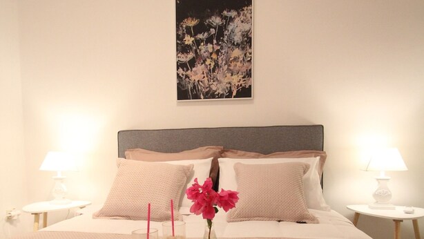 Een keurig opgemaakt bed met een dienblad vol ontbijtartikelen, waaronder twee drankjes en een vaas met bloemen, in een goed verlichte kamer met een strak, minimalistisch design.