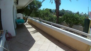 Un balcon avec une table et des chaises, une balustrade et une vue sur les arbres et les bâtiments.
