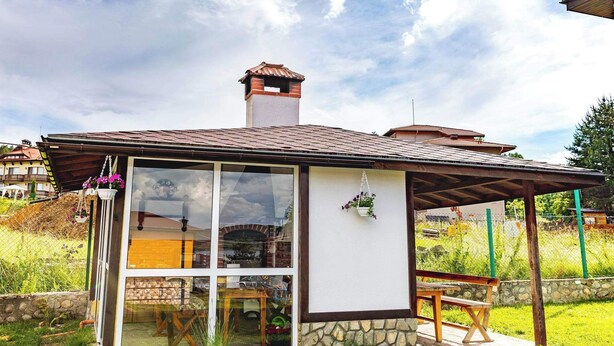 Il s’agit d’un petit bâtiment d’un seul étage, doté d’un toit en tuiles et de fondations en pierre. On y trouve une porte en verre qui donne sur un espace intérieur, ainsi qu’un banc en bois et une table à l’extérieur.