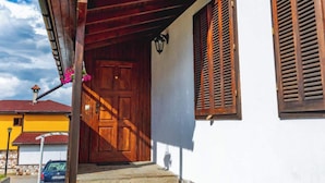 Un escalier en pierre menant à une porte en bois avec des volets, un ciel dégagé et une voiture garée au loin.
