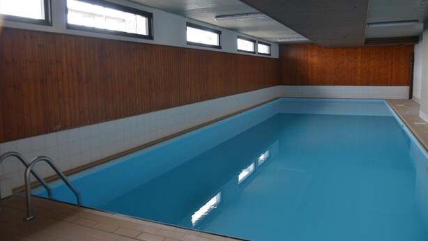 An indoor swimming pool with wooden paneling, a tiled floor, and a metal ladder.