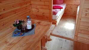 L’intérieur d’un chalet en bois, avec un banc, une table sur laquelle se trouvent une bouteille et des collations, et un lit avec un oreiller rouge.